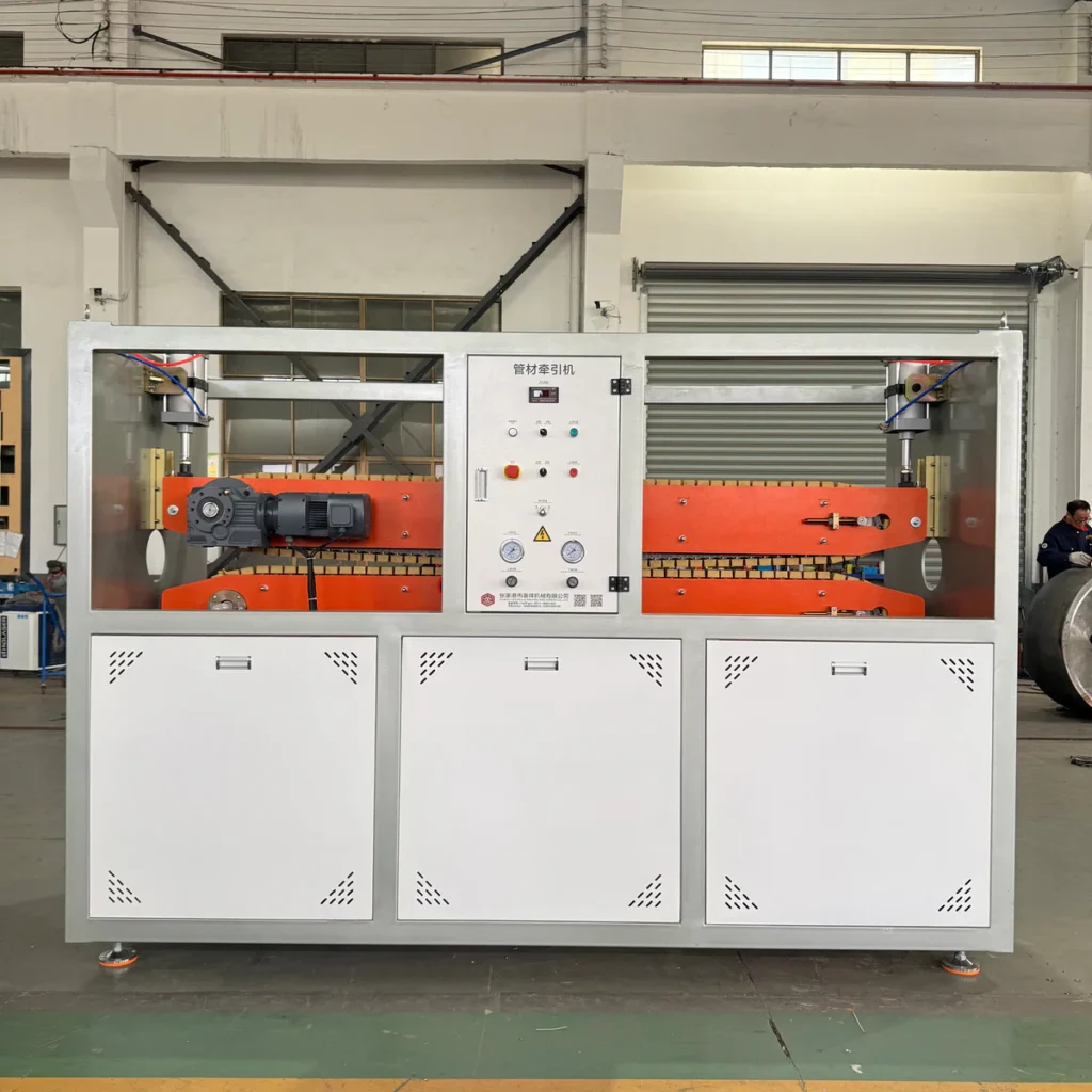 Front view of a double caterpillar haul-off machine with orange belt tracks and a control panel, set in a factory workshop