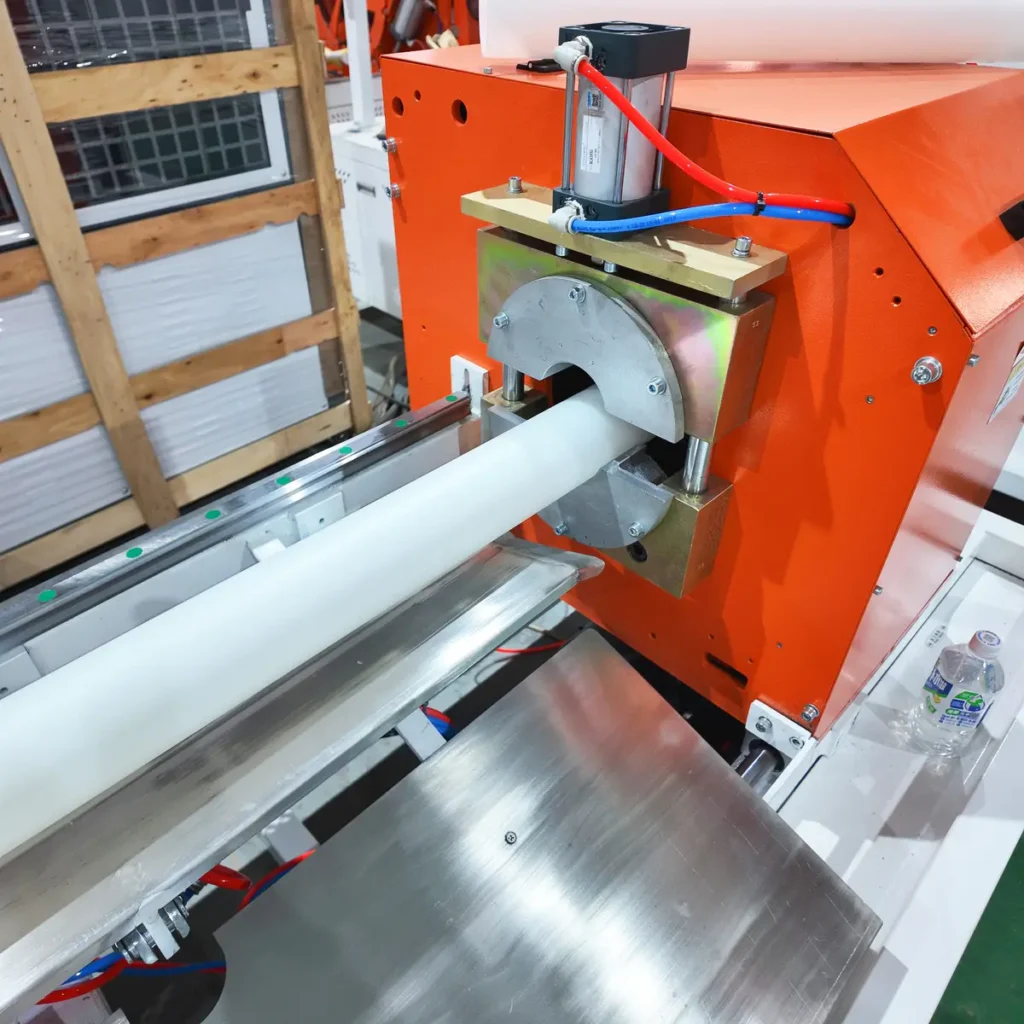 White plastic pipe exiting an orange dust-free pipe cutting machine on a factory floor