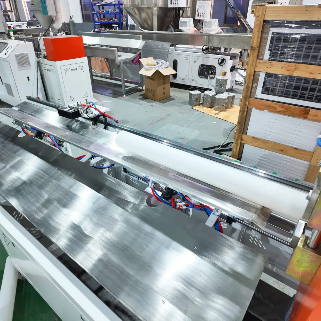 A white plastic pipe moves through a dustless pipe cutter on an extrusion line in a factory setting