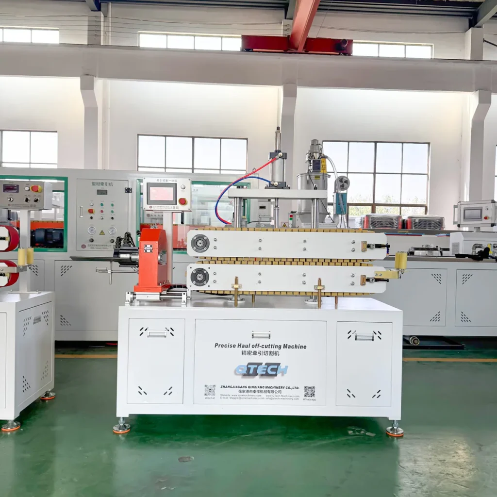 A white integrated haul-off and cutting machine with control panels stands in a well-lit factory workshop among other