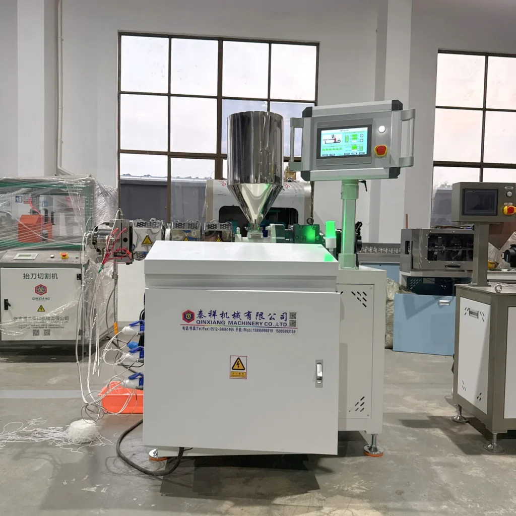 A lab extruder with a stainless steel hopper and touchscreen control panel installed in a factory workshop setting