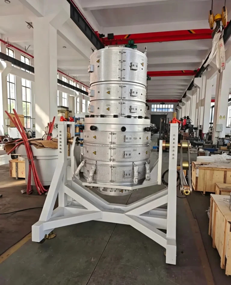 Large cylindrical segmented heating unit with cables and warning labels standing on a sturdy frame in a factory workshop