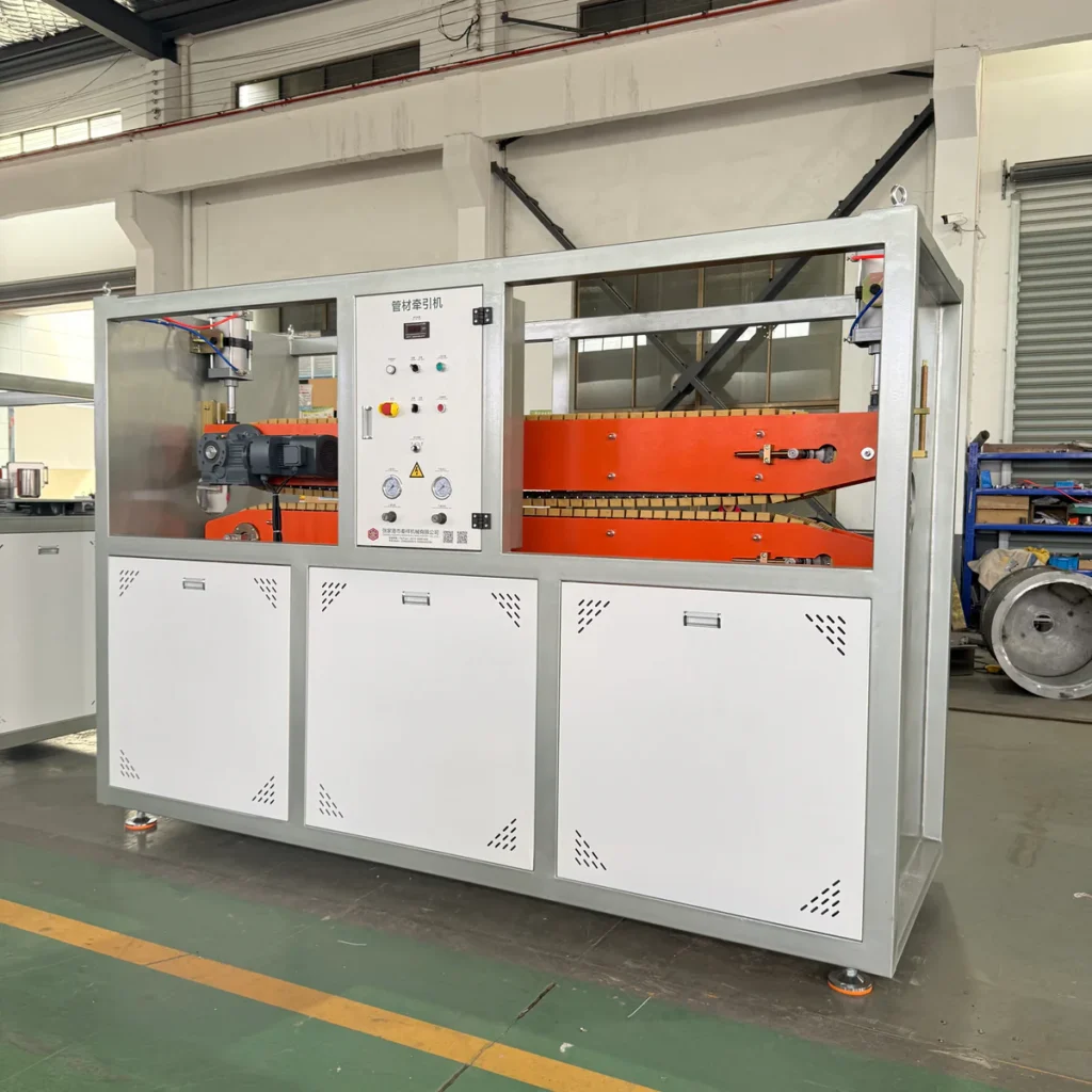 Factory floor view of a twin track haul-off machine with an orange belt and control panel in the foreground