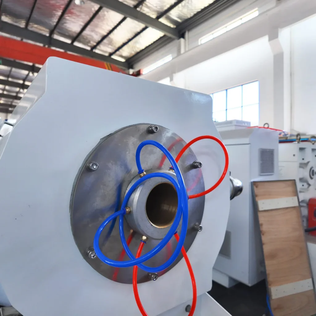 Closeup view of an extrusion die head with blue and red cooling water hoses attached in a factory workshop