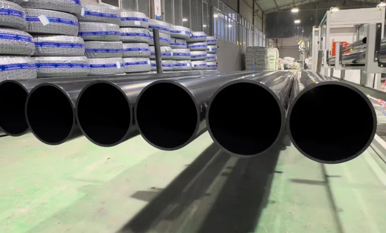 Large black plastic pipes emerging from machinery on a factory floor with stacked material bags in the background