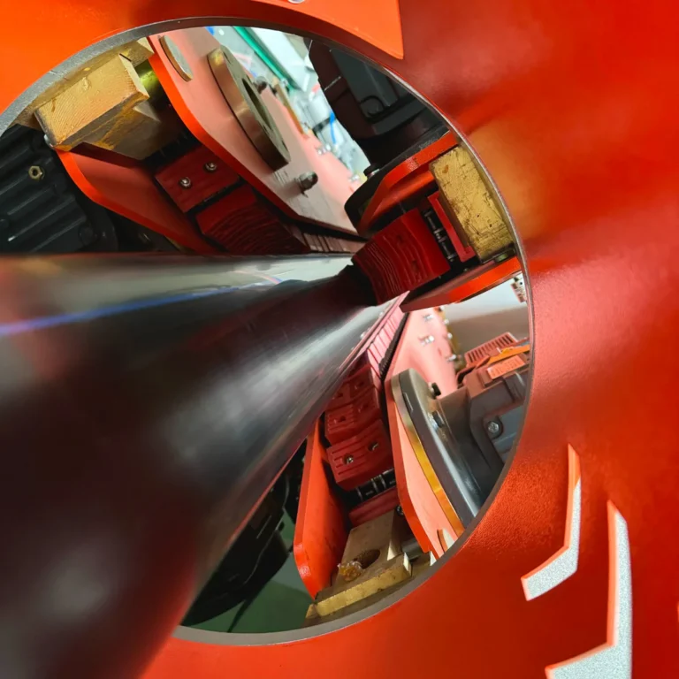 Closeup view of a black plastic pipe moving through a red haul-off unit on an extrusion line