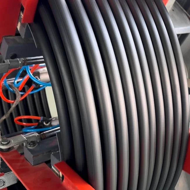 Closeup of black HDPE pipe being coiled by a machine with visible pneumatic lines and red frame