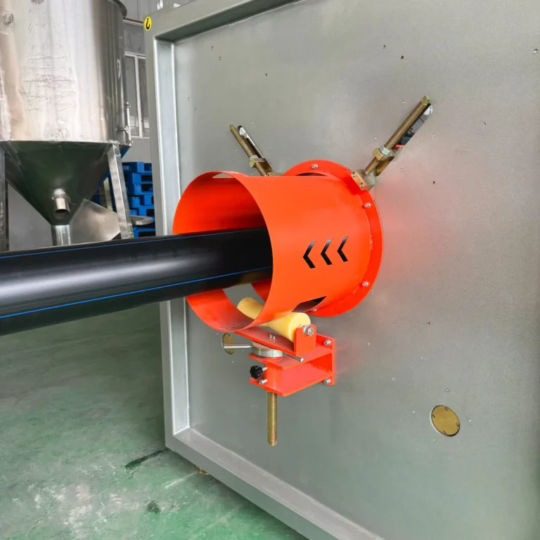 Black plastic pipe emerging from an orange guiding unit on an extrusion line in a factory setting