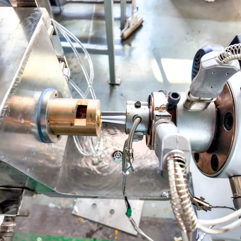 Closeup of an extrusion die head with heater and sensor wiring attached on a factory floor