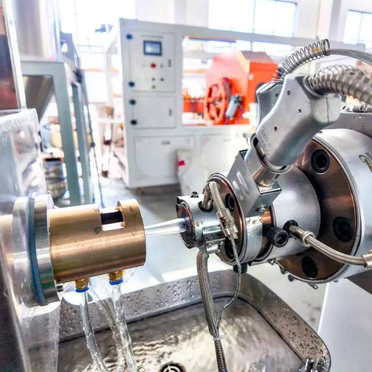 Extruder die head forming a round plastic tube with water cooling on a factory floor
