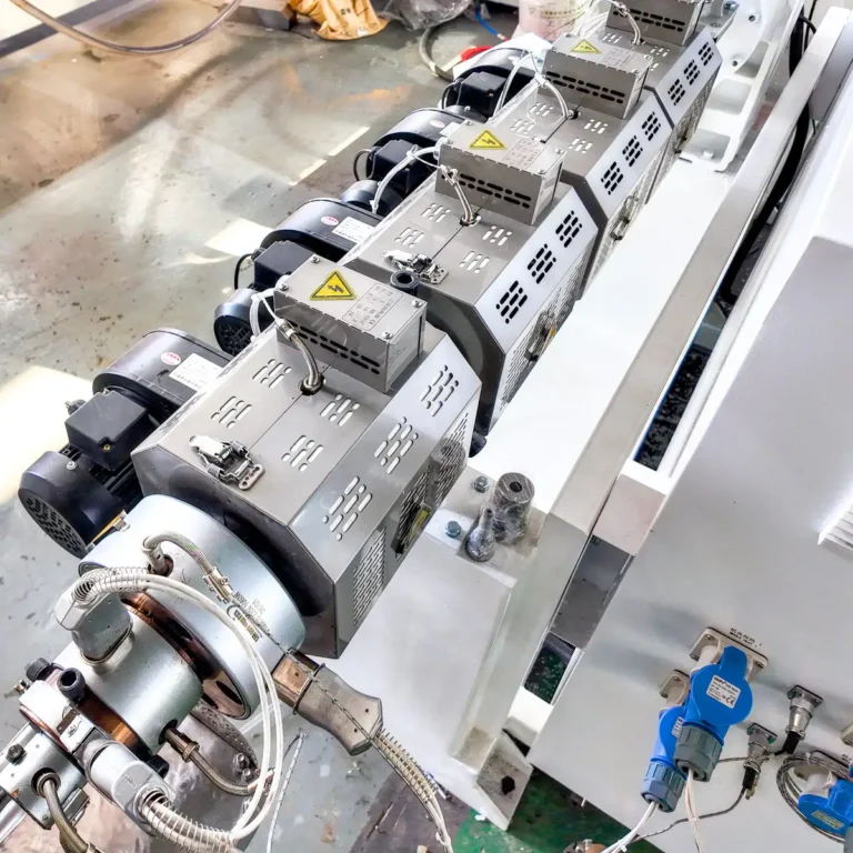 Close-up of an extruder barrel with heater bands, wiring, and sensors in a factory environment