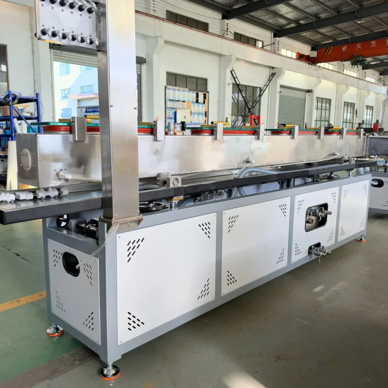 A long stainless steel cooling tank with multiple plastic profiles exiting, installed in a factory workshop with an overhead