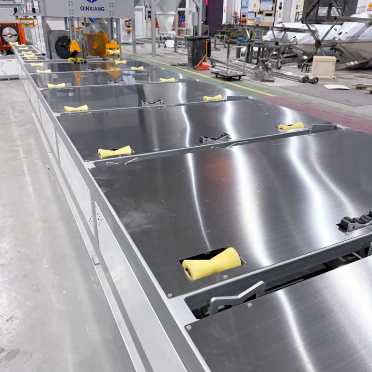 A long stainless steel calibration or cooling table with yellow rollers is set up in a factory workshop