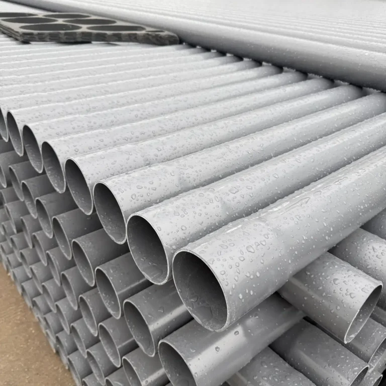 Close-up view of stacked grey PVC pipes with water droplets on their surfaces outdoors