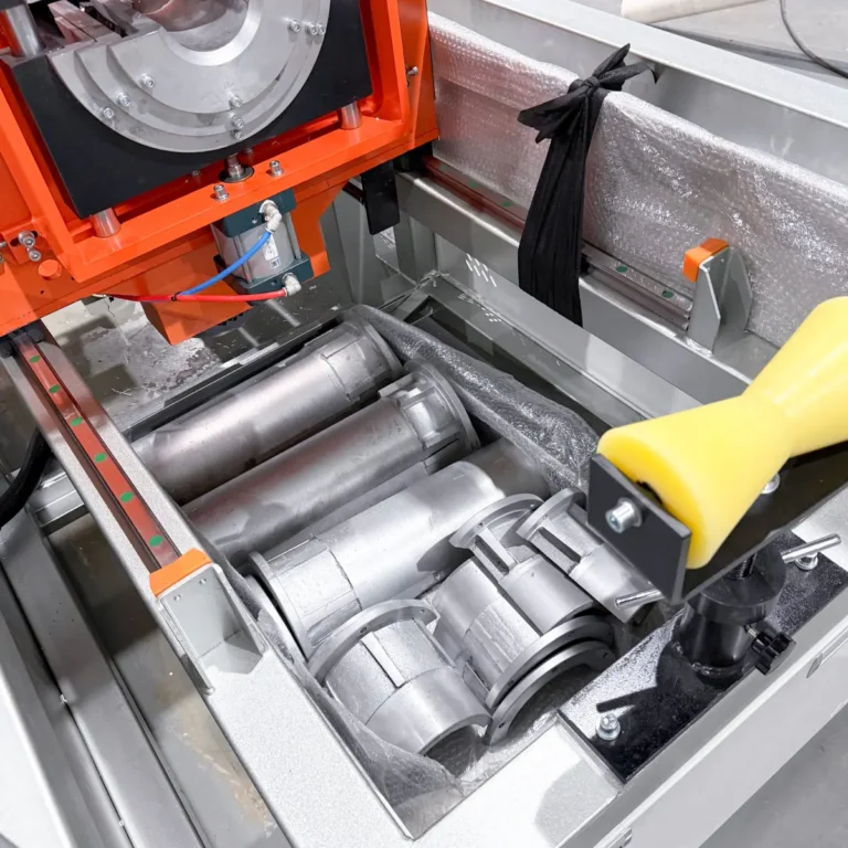 Closeup of a metal roller assembly and orange machine frame on a workshop floor, with no pipes visible