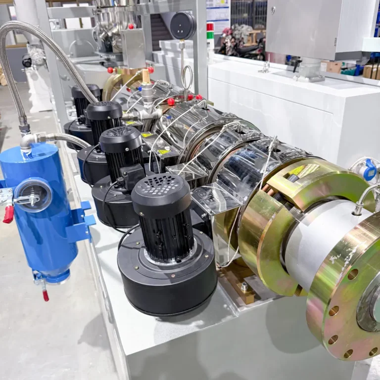 Closeup view of a plastic extrusion machine with barrel heaters, motors, and piping on a factory floor