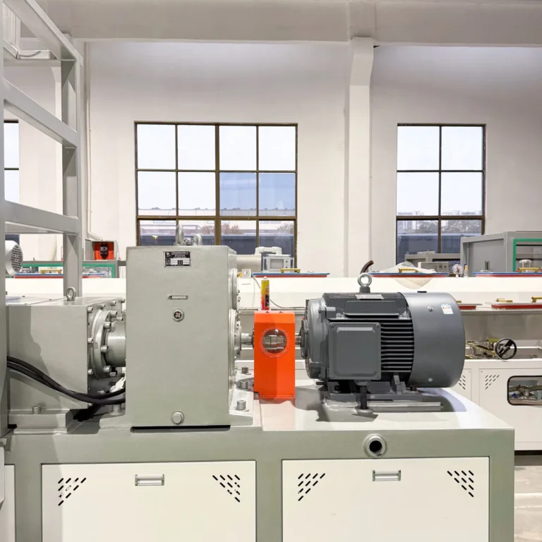 Extruder motor and gearbox assembly mounted on a machine base in a factory workshop with other machinery in the background