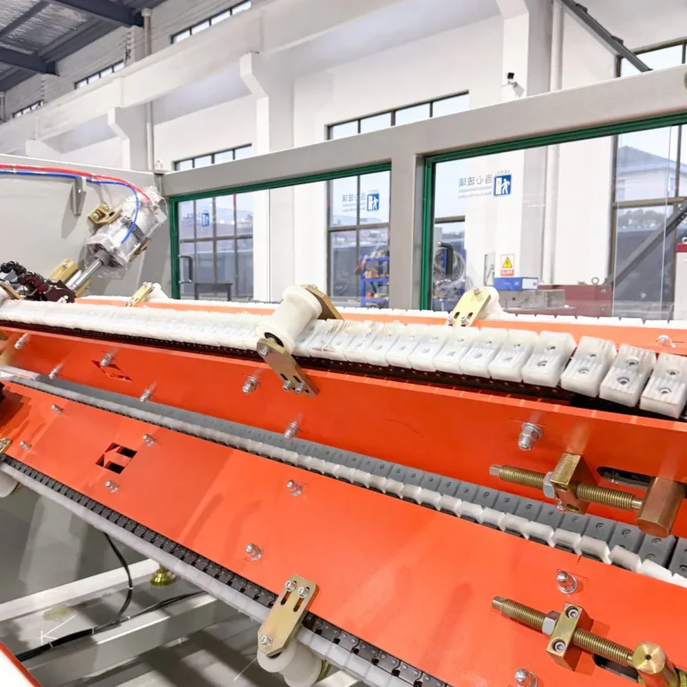 Closeup view of a haul-off machine with orange covers and white caterpillar tracks on a factory floor