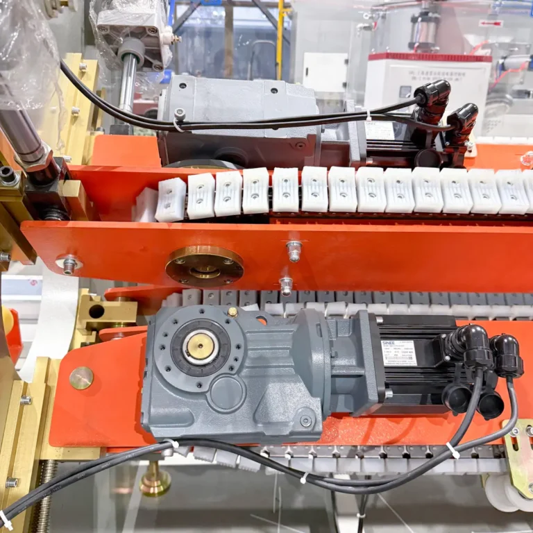Closeup view of a servo haul-off unit with gearmotors and white rubber blocks on an orange frame in a factory setting