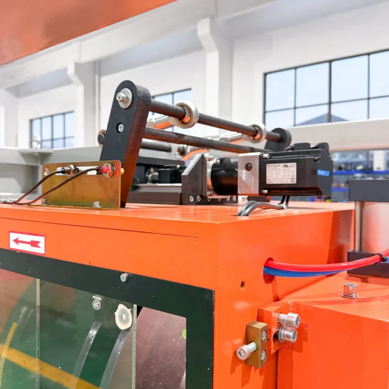 Closeup of an orange extrusion machine component with rollers and a servo motor on a factory floor