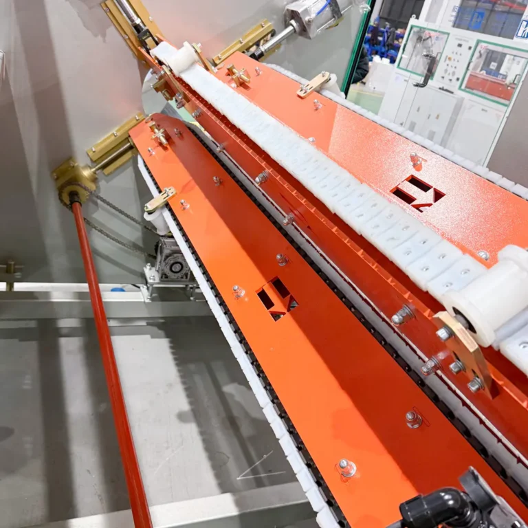 Closeup view of a haul-off unit gripping a red plastic pipe in a factory environment