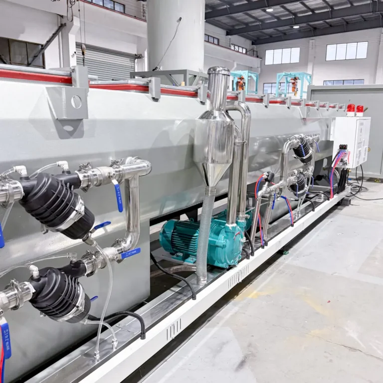 Closeup view of a cooling or calibration tank with stainless steel piping, pumps, and valves installed on a factory floor