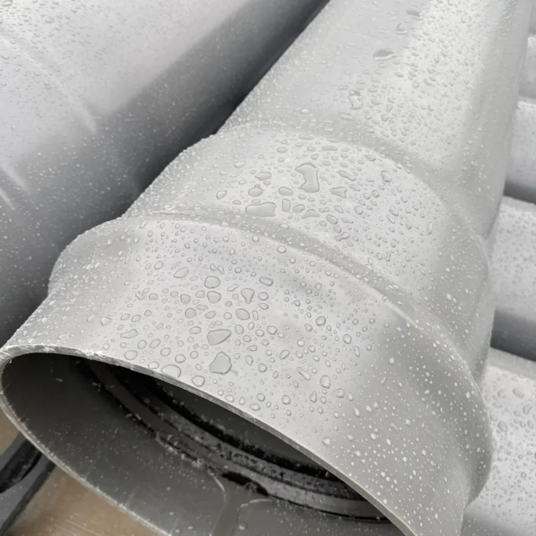 Close-up of stacked grey plastic pipes with belled ends and water droplets on the surface