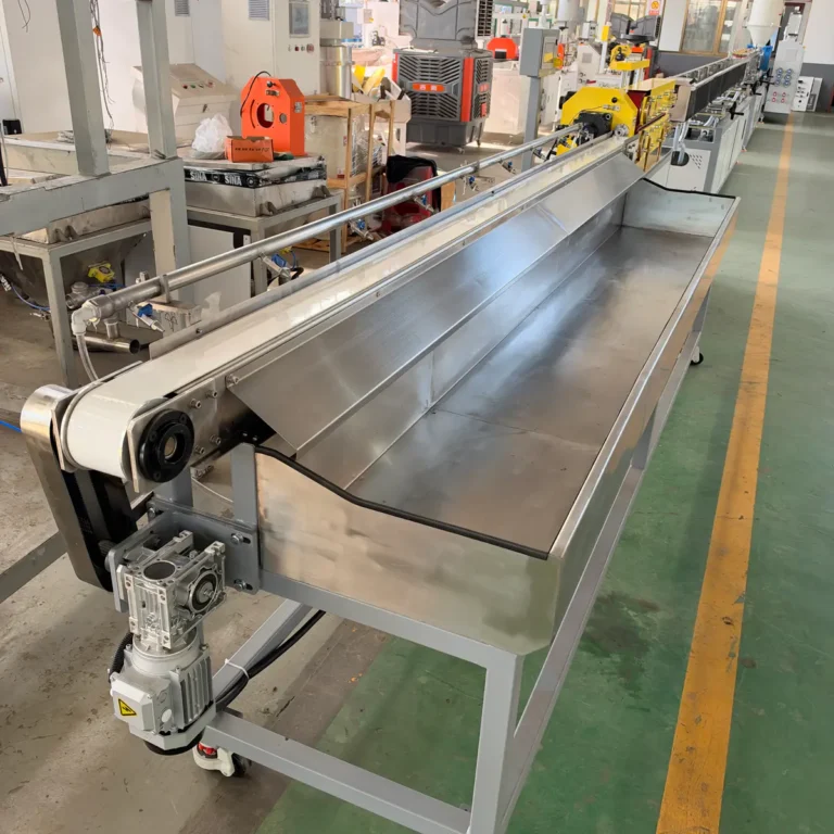 A stainless steel collection trough with motorized components is installed along a plastic extrusion line in a factory