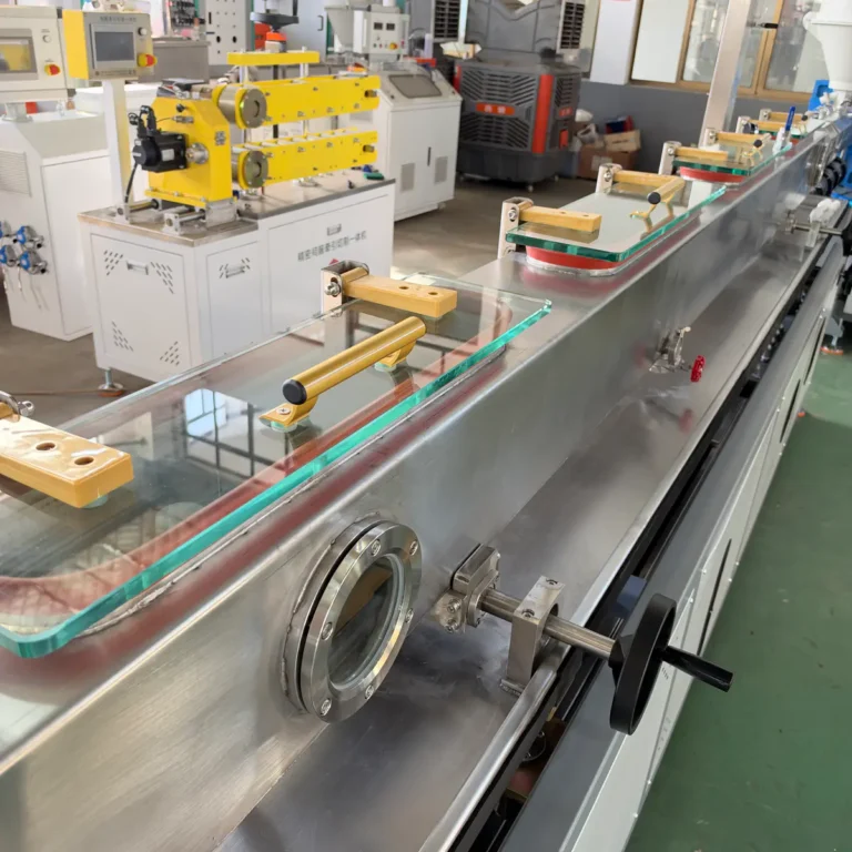 Stainless steel vacuum sizing water tank with glass covers and adjustment handles in a factory workshop, with a yellow